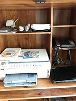 HP Photosmart C6280 all-in-one printer, Sony Blu-ray player, Panasonic corded phone, and calculator arranged on wooden shelf