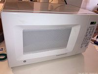 Front view of white General Electric microwave oven showing window and control panel with buttons and digital display.