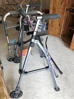 Photo showing two metal walkers, one with wheels and one foldable, in room
