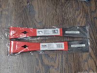 Two 10 inch mini pry bars in plastic packaging showing the red handle areas and black metal ends on a wooden surface.
