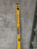 Long yellow 48 inch aluminum box level standing vertically against a concrete wall, showing multiple bubble vials and black end caps.