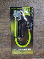 Front view of packaged Flexzilla tire inflator showing metal body, pressure gauge, and bright green hose.