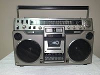 Front view showing dual speakers, cassette deck, push-button controls and telescoping handle
