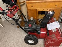 Side view of entire snow thrower showing engine, wheels, handle and manual
