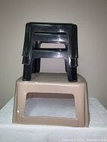 Stacked black and beige plastic step stools showing size difference and condition