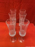 Six clear crystal champagne flutes standing upright on a red surface, showing tops and decorative cut pattern at the base of the bowl.