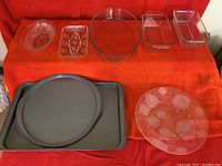Photo showing all bakeware and decorative glass dishes on orange cloth, including metal baking pans, glass loaf pans, Pyrex oval dish, and decorative plates.
