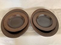 Six brown Wedgwood dishes arranged in two stacks, showing the embossed geometric patterned rims and matte finish.