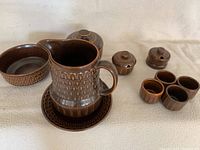 Overall set of brown Wedgwood Pennine pottery pieces showing milk jug, bread plate, fruit bowl, 4 egg cups, covered sugar bowl and two mustard pots with lids.