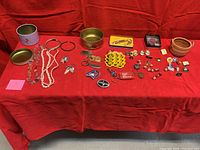 Full spread of items on red cloth including tins, jewelry, pins, and key chains