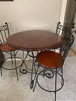 Round wooden top counter height table with cast iron legs and three matching cast iron and wood chairs arranged around it on carpeted floor.