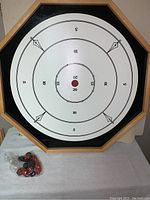 Octagonal Crokinole board with numbered scoring rings, visible red and black pucks in plastic bag.