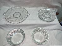 Four different glass plates and bowls displayed on a light towel: top left is a bead edged plate, top right is a round etched plate with floral and corn flour design, bottom left and right are two small glass bowls.