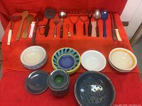 All kitchen utensils and assorted bowls arranged on a red cloth with visible chips on some bowls.