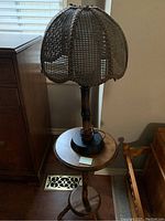 Lamp on wooden pedestal side table showing mesh-style lampshade and round tabletop