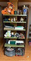 Metal shelf with six shelves containing assorted stuffed animals, kitchenware, paper pads, and figurines as described.