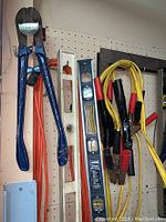Photo showing blue bolt cutters, two spirit levels, yellow jumper cables, and orange extension cords on beige pegboard wall.