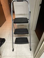 Front view of the 3-step folding stepstool showing black textured steps and silver metal frame with handle.