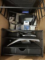 Black metal mesh drawer organizer filled with assorted office supplies, view from above