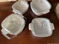 Top view of four Corningware square dishes each with glass lids, arranged on wooden surface with metal stand included.