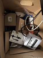 Box filled with various cables, boxes, and battery chargers showing cords and connectors