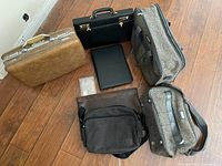 Front view of all items including brown and black briefcases, portfolio, black shoulder briefcase, and 2-piece grey luggage set