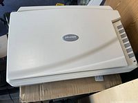 Closed white Plustek flatbed scanner showing top view with logo and side buttons.