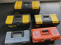 Five closed tool boxes arranged on the floor showing overall size and color variations among Stanley, Plano, and Ganchun brands.