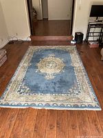 Full view of blue Persian-style rug on hardwood floor showing central floral medallion and border design.