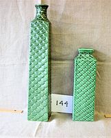 View showing both the tall and short green ceramic vases with scaled texture against a fabric backdrop