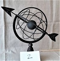Front view of the black metal armillary sphere with arrow through the center and decorative base.