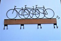 Full front view of the bicycle wall hooks mounted on a white background showing the metal bicycle design and wood panel base with four metal hooks below.
