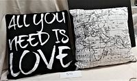 Two cushions placed side by side on a black chair, showing the full design of both cushions: text and map