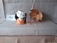 Photo showing ceramic girl planter and metal floral umbrella side by side on fabric background.