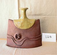 Front and side view of the ceramic vase showing the yellow-green glazed partial top and the reddish-brown unglazed textured lower portion with floral detail.