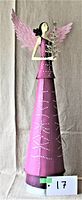 Front view of tall metal angel with pink wings and purple gown holding small Christmas tree, photographed against grey fabric background with size marker.
