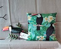 Photo showing the metal toucan figurine and the toucan print cushion side by side on a neutral surface.