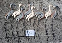 Full view of ten metal wading herons arranged on the ground, showing variety of metallic colors and slender metal legs.