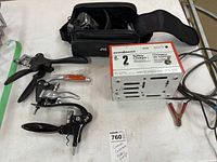 All items on white surface showing JVC camera inside soft carrying case, three corkscrews, and Motomaster battery charger with cables and clamps.