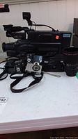 Samsung VHS movie camera HC966349 model on a table next to several compact cameras and a telephoto lens