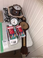 Overview of all lot items including multiple clocks, barometer, and string lights boxes placed on a white table.