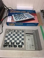 Photo showing the computerized chess set laid out on a flat surface with chess pieces positioned on the board near the original box and power cord visible.