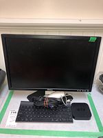 Full view of Dell monitor, Logitech keyboard, Apple TV device, white Apple mouse, and cables on table.