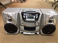 Front view of the JVC portable stereo system with central main unit and two silver detachable speakers.
