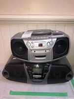 Two portable stereos stacked. One silver with CD player controls and speakers. One black with cassette and digital display.