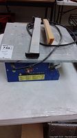 Full view of the portable tile saw on table, showing the cutting surface, power cord, and adjustable components.
