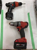 Shows the two battery operated drills side by side on a white surface; top is Black & Decker, bottom is Milwaukee M18 with attached battery pack