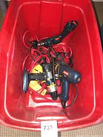Photo showing multiple corded electric drills in a red bin, different colors and models