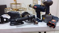 Overview photo showing all four power tools on a table including sander and three cordless drills.