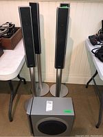 Four tall pedestal Sony speakers with black mesh grille and silver stands alongside one grey Sony subwoofer with a large black circular speaker grille on the front.